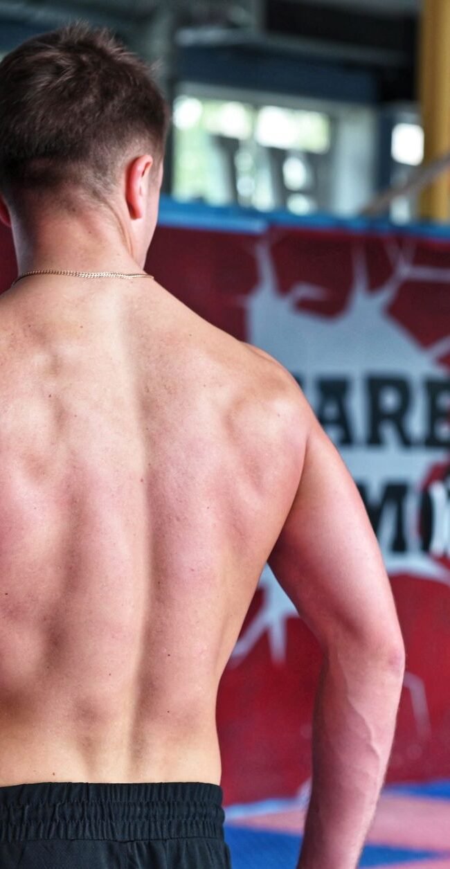Shirtless man showcasing muscular back indoors in fitness gym.