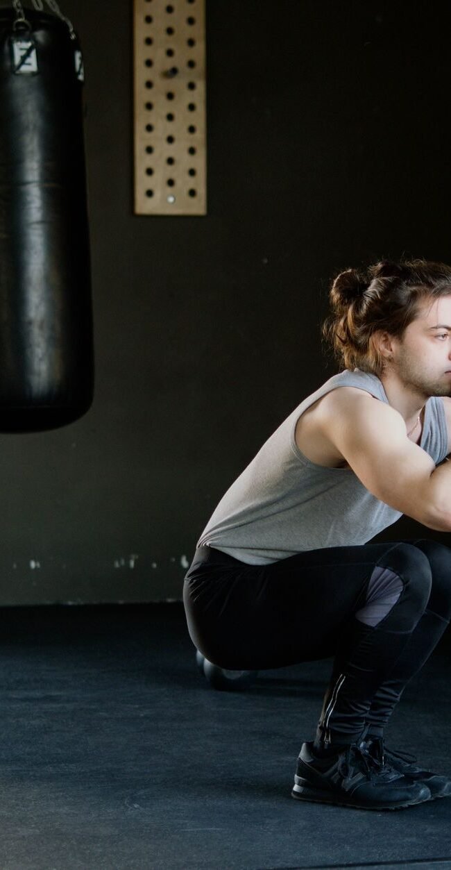 A man is doing squats in a gym with a punching bag. The setting appears stylish and focused on fitness.
