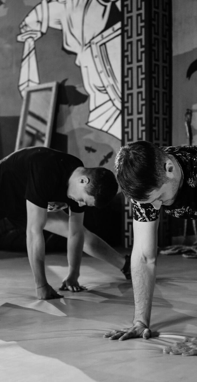 Two men stretching inside a gym, preparing for MMA training in a grayscale setting.