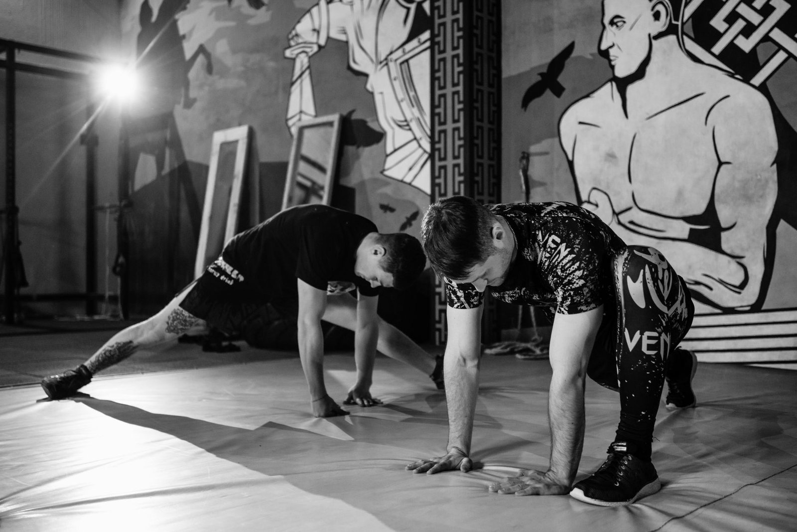 Two men stretching inside a gym, preparing for MMA training in a grayscale setting.