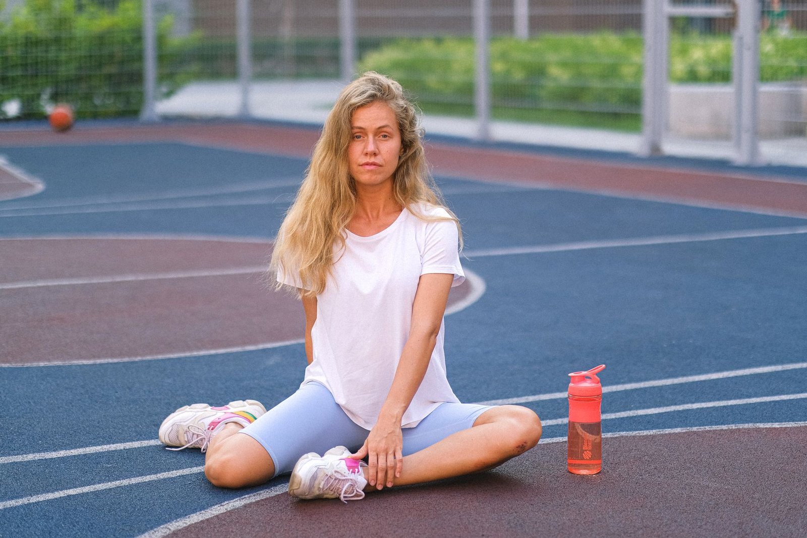 Full length of young serious woman in sportswear exercising on court near bottle with water in daylight and looking at c