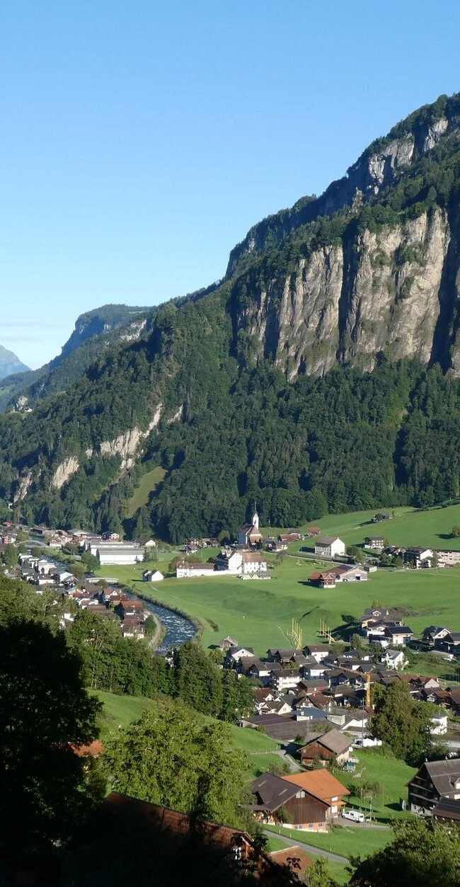 Scenic view of a Swiss village nestled in a lush mountain valley under a clear blue sky.