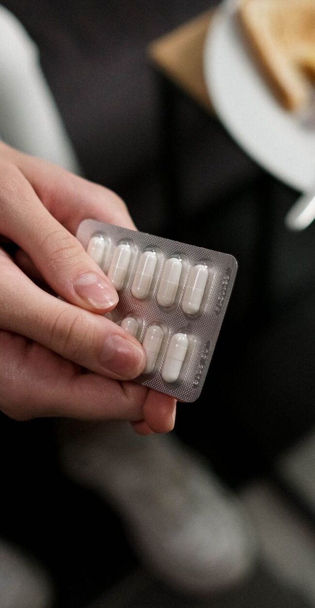 Close-up of a person holding a blister pack of pills with breakfast in the background, indicating medication and daily r