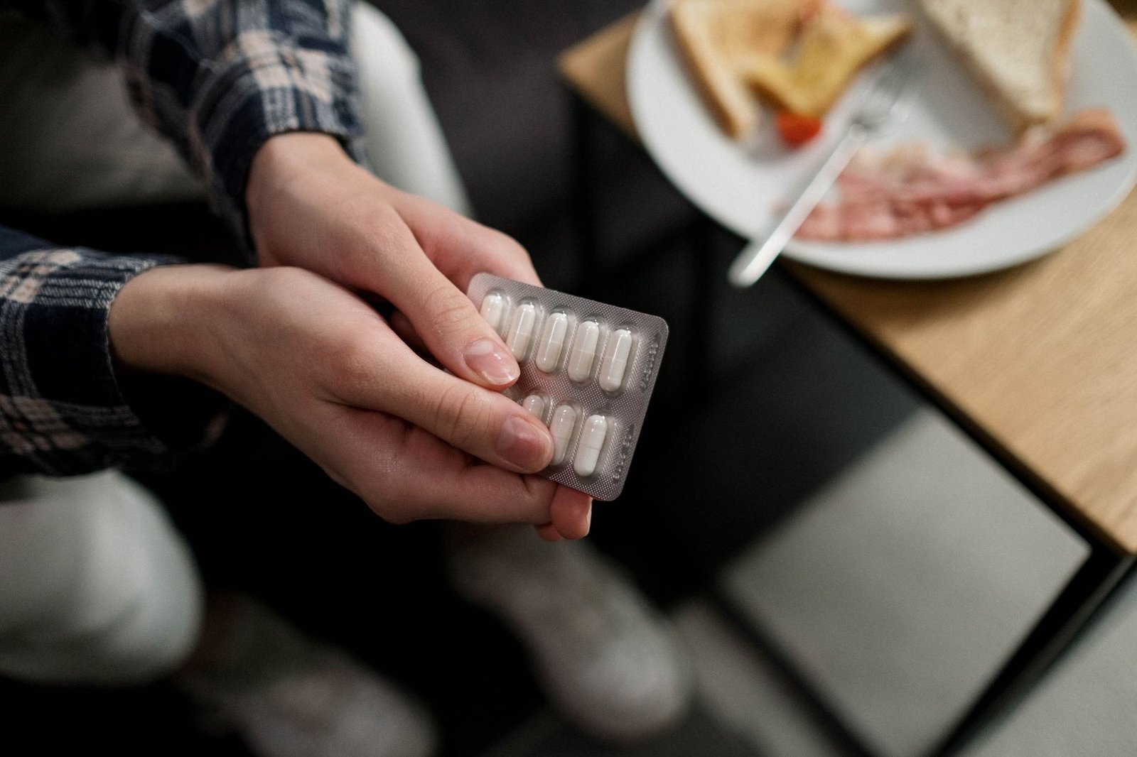 Close-up of a person holding a blister pack of pills with breakfast in the background, indicating medication and daily r