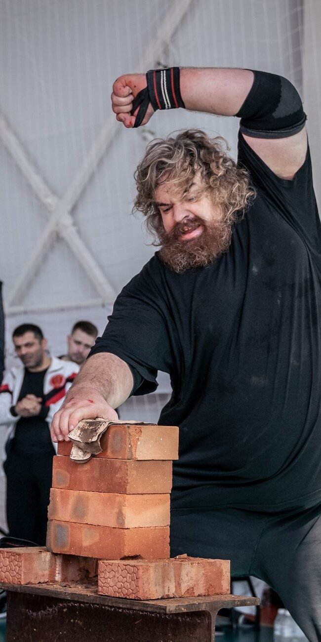 A strongman breaks bricks with his hand at an indoor sports competition event.