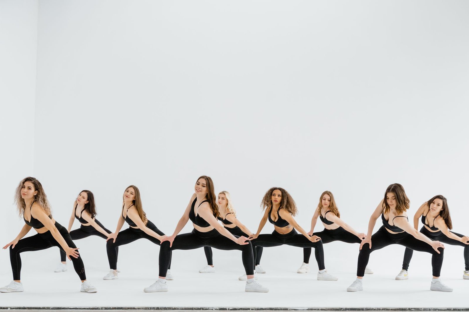 A dynamic group of women performing a synchronized dance routine in sportswear on a white background.