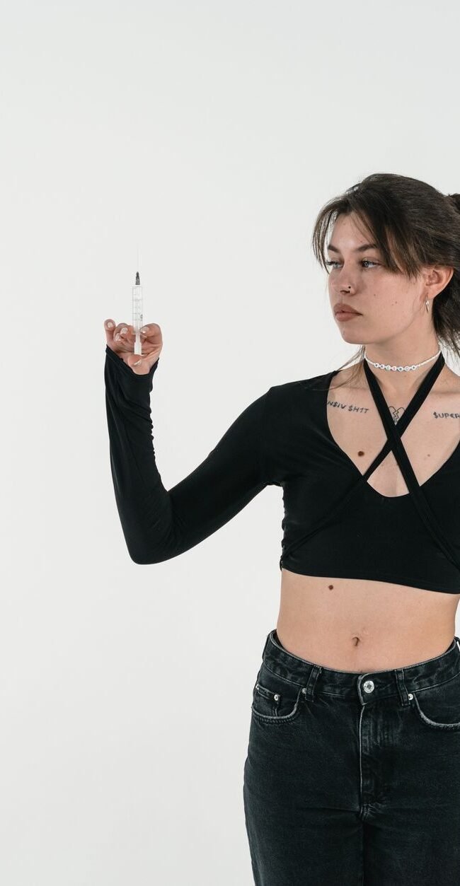 A young woman in fashionable attire holds a syringe, symbolizing health themes.