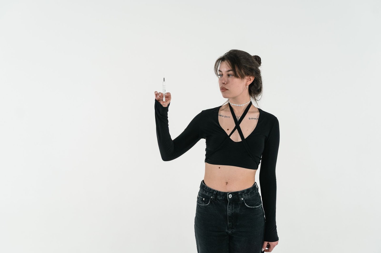 A young woman in fashionable attire holds a syringe, symbolizing health themes.