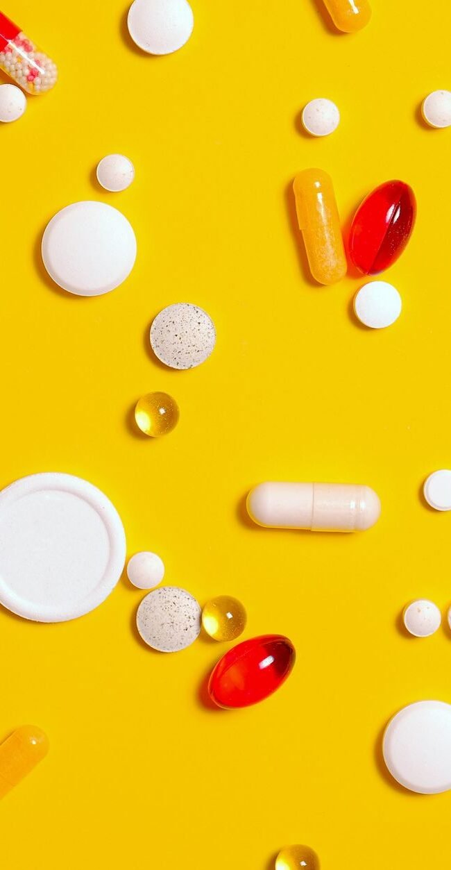 A variety of pills and capsules scattered on a vibrant yellow backdrop, emphasizing health and medicine.