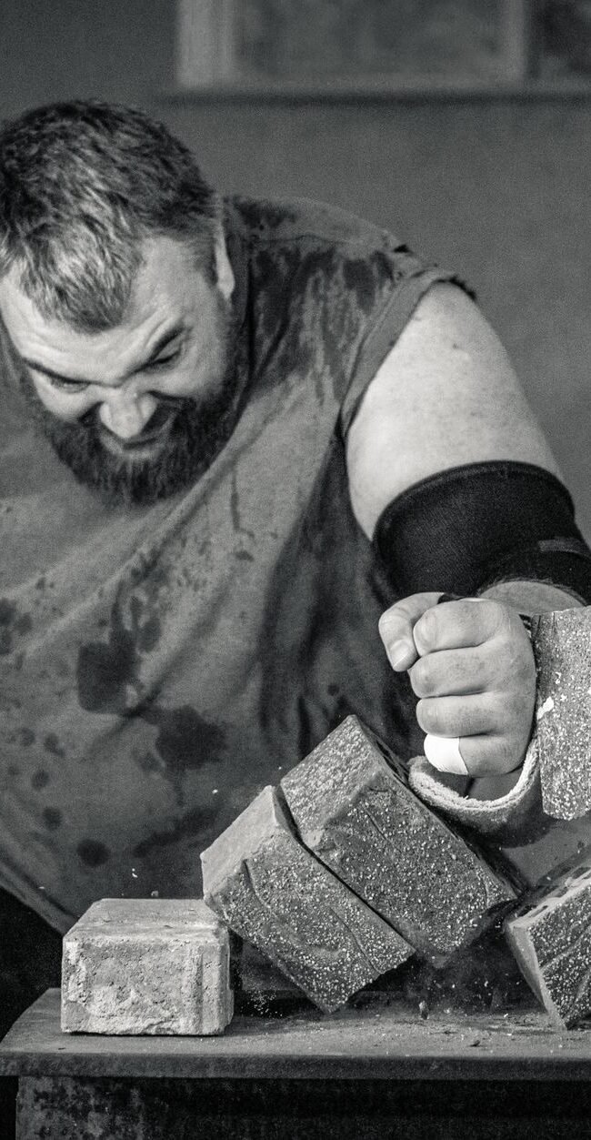 A powerful image of a strongman smashing concrete blocks with his fist, showcasing strength and determination.